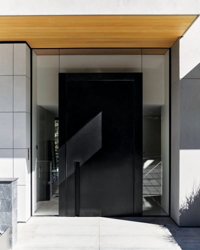 An exterior pivot door in Vail is made from blackened galvanized steel. A recessed handle is built into the door, which is completely surrounded by glass with no structural components at the side or the top.