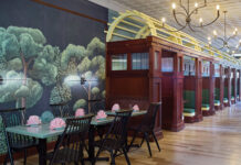 Inside the Artful Interiors of Rōmyō on Larimer Square Interior of Rōmyō restaurant in Denver featuring custom wooden train-inspired booths, green upholstered seating, whimsical forest wallpaper, and elegant chandeliers.