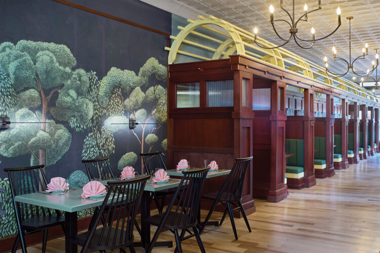 Interior of Rōmyō restaurant in Denver featuring custom wooden train-inspired booths, green upholstered seating, whimsical forest wallpaper, and elegant chandeliers.