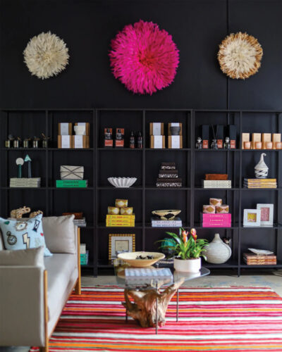 nterior of The Refinery in Boulder featuring black shelving filled with curated home décor, colorful feather wall art, a cream sofa, a glass coffee table, and a vibrant striped rug.