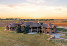 What Denver Homebuyers Should Know About Today’s Real Estate Market Aerial view of a sprawling luxury home with stone accents, a tiled roof, and expansive grounds surrounded by farmland at sunset.